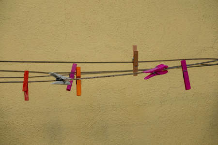 A closeup shot of several multicolored clothespins attached to metal cords behind a yellow wall