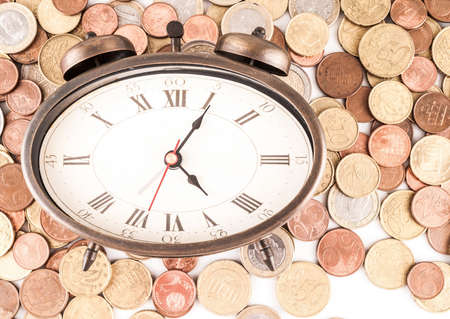 An aerial shot of a vintage alarm clock laid in a surface full of coins