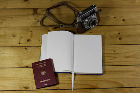 A high angle shot of an open notebook next to a passport and a camera on a wooden surfaceの写真素材