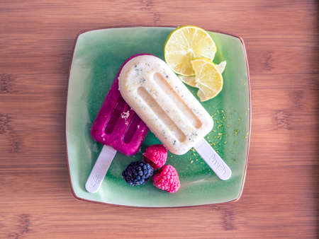 A high angle shot of two delicious ice lolly with fruits in a green plate on a wooden table