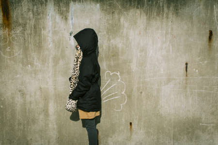 A person with a black coat standing in front of an old painted wall