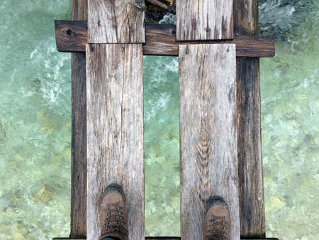 An overhead shot of a person standing on wooden boards above the water