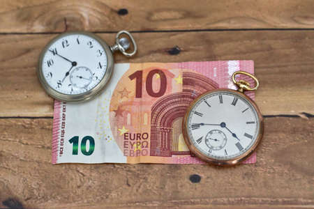 A high angle shot of two vintage clocks on a ten Euro on a wooden table