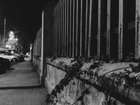 A grey-scale shot of an old building with a metal fence in the streets at nightの写真素材