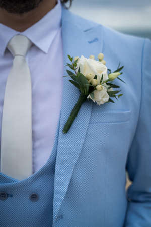 A closeup shot of grooms light blue suit and a small white flower on itの写真素材