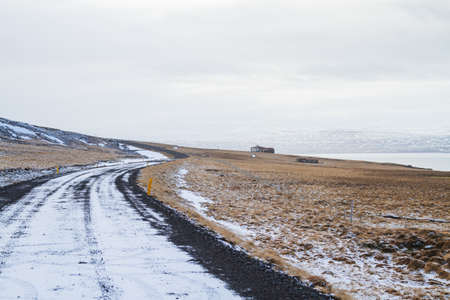 A road surrounded by a field covered in the grass and snow under a cloudy sky in Iceland
