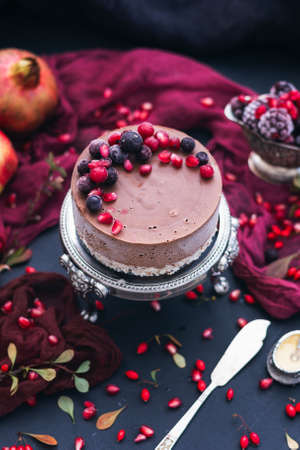 A vertical shot of a chocolate cake with fresh berries and pomegranate seeds on itの写真素材