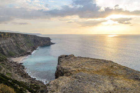 The sea surrounded by rocks covered in mosses under a cloudy sky during a beautiful sunset