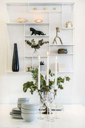 A vertical shot of a table setting with candles, plates and glass cups near a shelf
