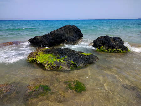 A beautiful shot of black rocks lying next to the beach in Ibiza, Spain