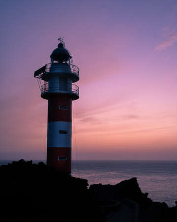 A vertical shot of a lighthouse on the shore of the sea with the purple sky in the backgroundの写真素材