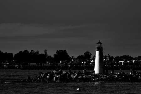 A grayscale shot of lighthouse beacon on the shore of the seaの写真素材