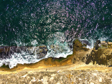 A high angle shot from the top of the cliff with sea waves hitting on the rock
