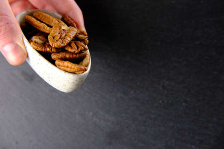 Three fingers are holding a white plate with pecans on dark background