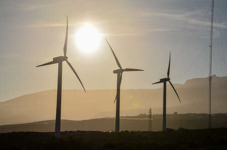 A silhouette shot of windmills with a glowing sun in the background