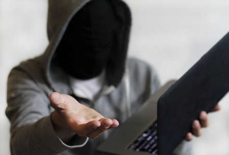 A mysterious male holding a laptop with his hand towards the camera