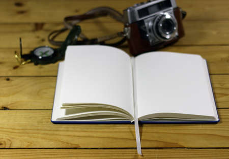 An open notebook next to a watch and camera on a wooden surfaceの写真素材