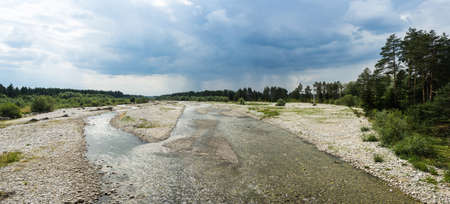 A panoramic shot of a shallow stream of water surrounded by trees and greenery