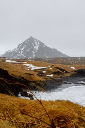 A vertical picture of a river surrounded by hills covered in the snow and greenery in Icelandの写真素材
