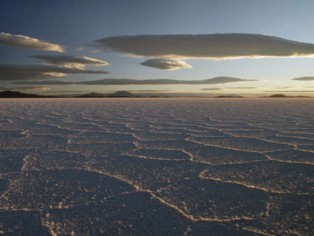 A low angle shot of a cracked ground with mountains in the distance under a blue skyの写真素材