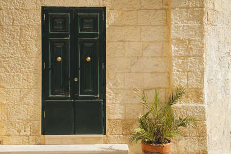 Facade of an old medieval Sandstone house with green doors and a potted plant in Malta in Valletta