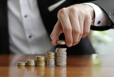 A selective focus shot of well-dressed male putting coins on the coin stack