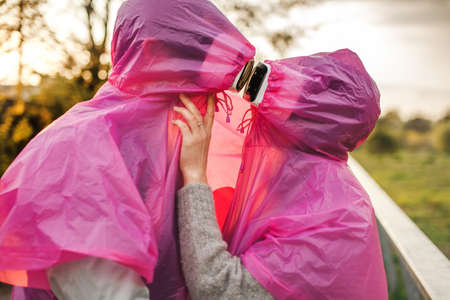A closeup shot of two people in pink plastic raincoats and VR headset kissing each other