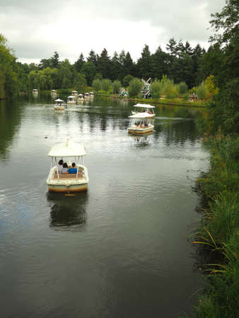 A vertical shot of people riding in white small boats in the lake surrounded by green plants with a cloudy gloomy skyの写真素材