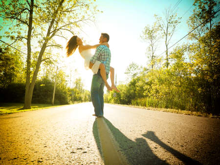 A man hugging a woman while standing on the road surrounded by greenery under the sunlightの写真素材