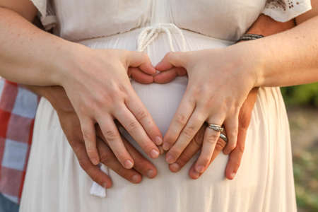 The married couple forming a heart shape with hands on the pregnant belly of the womanの写真素材