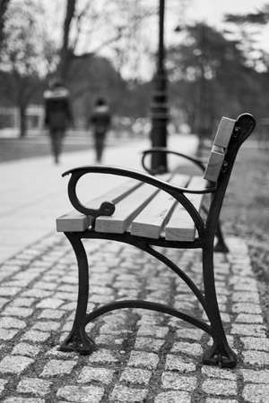 A vertical grayscale shot of a  bench in the park with a blurred backgroundの写真素材