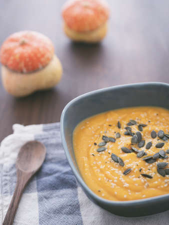 A bowl of pumpkin soup with two pumpkins and a wooden spoon on a wooden tableの写真素材
