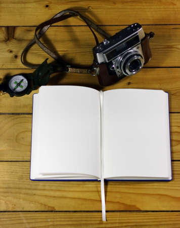 An open notebook next to a watch and camera on a wooden surfaceの写真素材