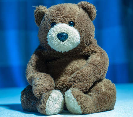 A cute brown stuffed bear toy on a blurred blue backgroundの写真素材