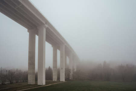 A concrete bridge on a hill surrounded by greenery covered in the fog under a cloudy skyの写真素材