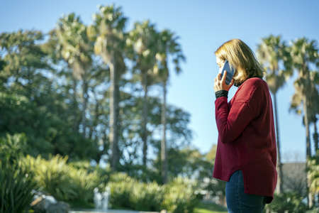 A mid shot of a woman on a phone call walking on a park with palm trees in the background