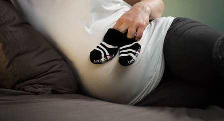 A beautiful shot of a pregnant woman in bed holding baby shoes in front of her bellyの写真素材