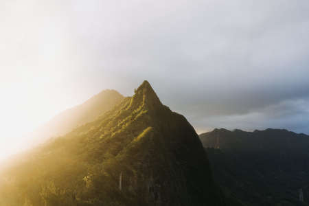 A beautiful shot of a steep mountain with a sunset in a cloudy blue sky in the backgroundの写真素材