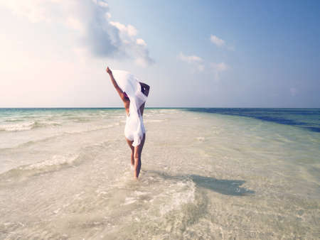A woman wearing a white dress and walking in the sea under the sunlight and a blue skyの写真素材