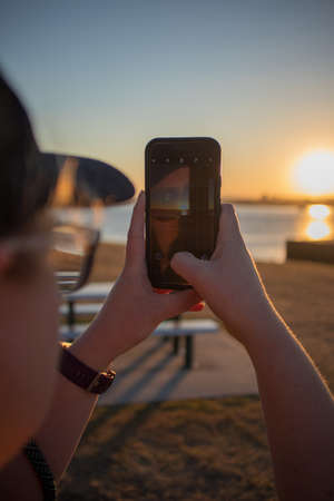 A closeup shot of a woman taking a picture of the sunsetの写真素材