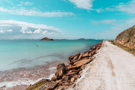 A road covered in the sand surrounded by the sea and rocks under a blue sky in Rio de Janeiroの写真素材