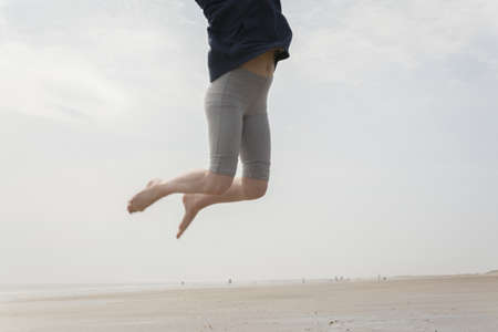 A low angle shot of a person jumping on the beach with a foggy backgroundの写真素材