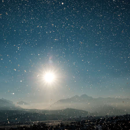 A picture of snowflakes with the sun and rocky mountains on the blurry backgroundの写真素材