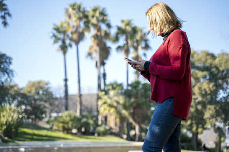 A low angle shot of a woman texting while walking on a park with palm trees in the background