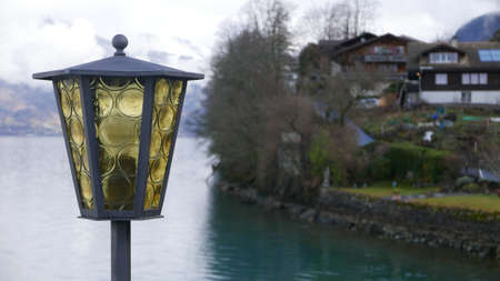 A selective shot of a yellow and black lamp with a river and a house in the backgroundの写真素材