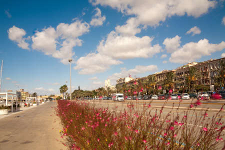A landscape shot of a wide road, different cars, large buildings on the side of the road with a...