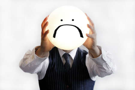 A well-dressed male holding a light with a sad face on itの写真素材