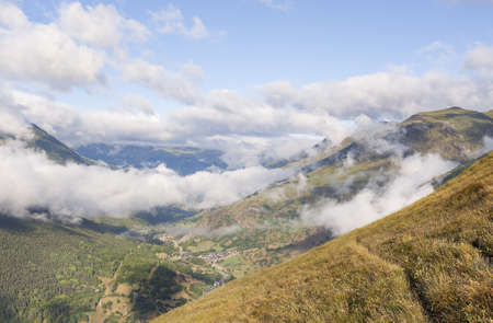 The mesmerizing view of the mountains covered by clouds in Val de Aran, Spain on a sunny dayの写真素材