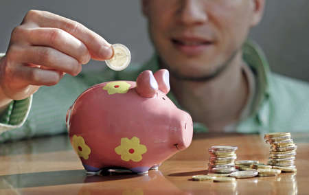 A selective focus shot of a male putting a coin in a piggy bank