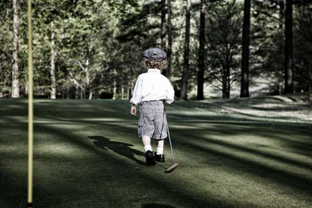A little boy golfing in a field surrounded by greenery under the sunlight